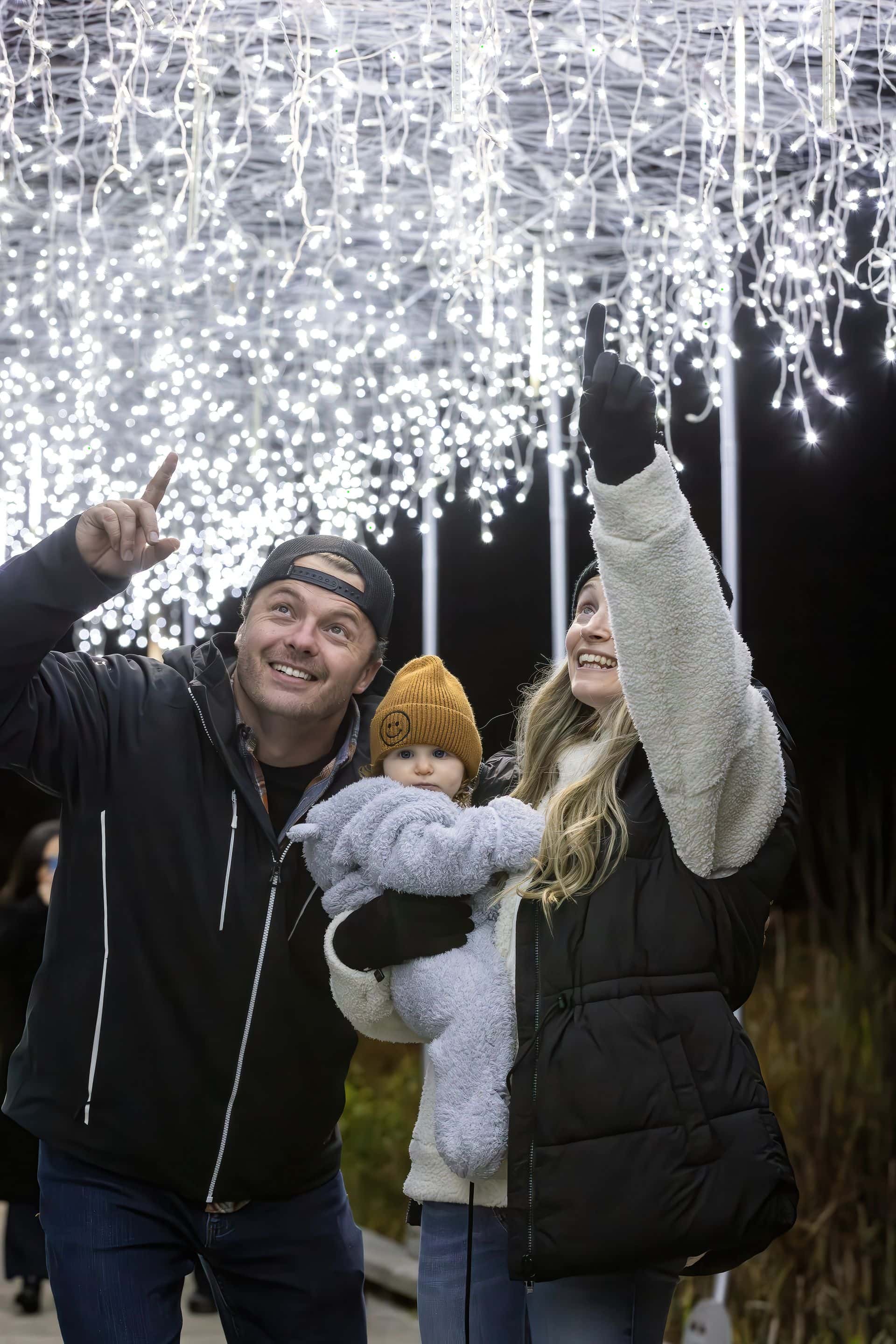 Parents with young baby pointing to show the baby the dangling Holiday Magic Lights.