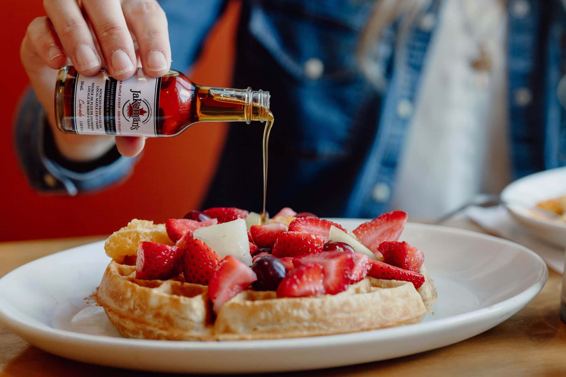 Hand pouring true Canadian Maple Syrup over a plate of warm waffles topped with fresh berries.