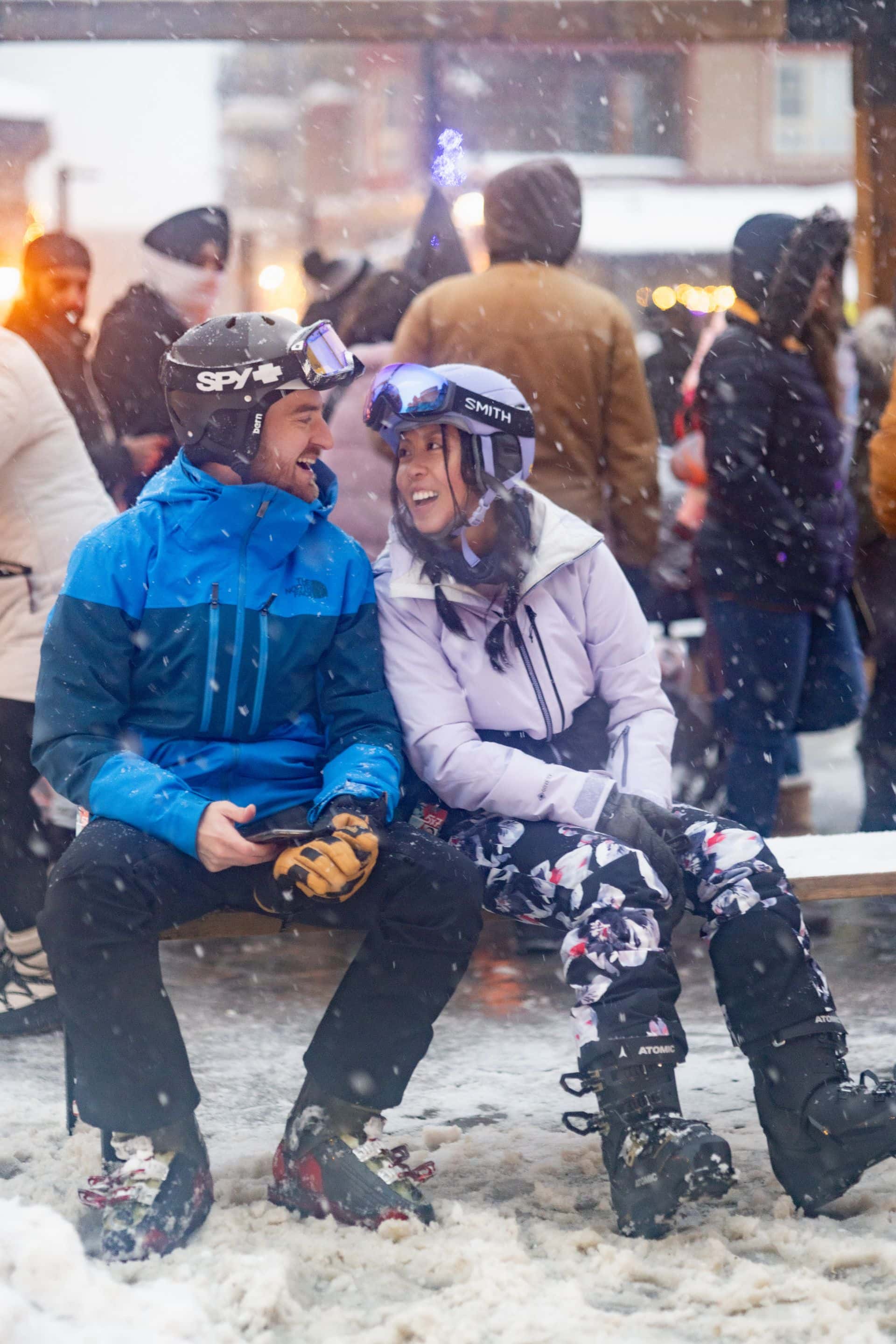 Couple leaning into each other as they sit on a bench in the Village after a day of skiing.
