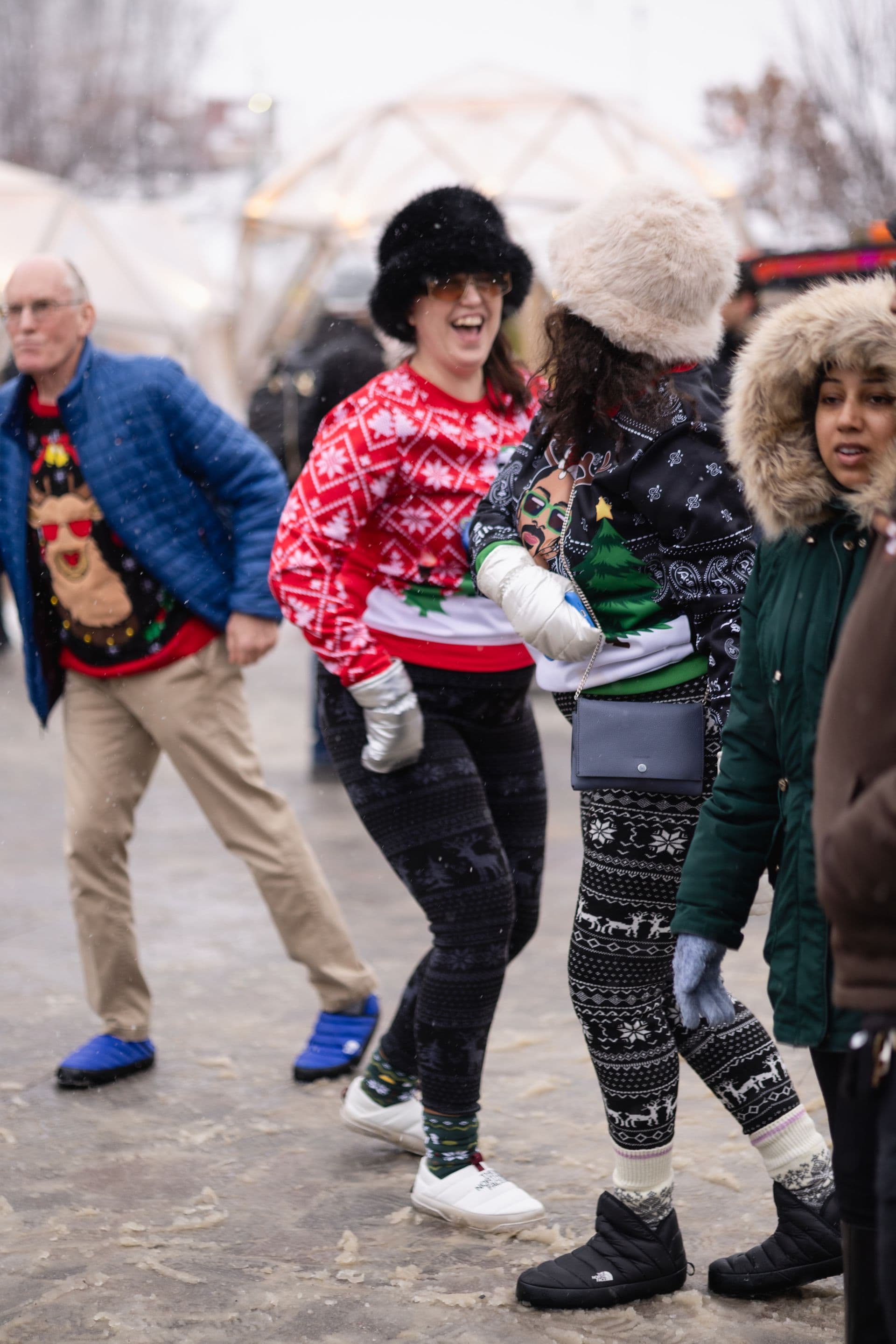 Friend dressed in Christmas sweaters and fur hats, dancing to Caribbean music in the Village events plaza.