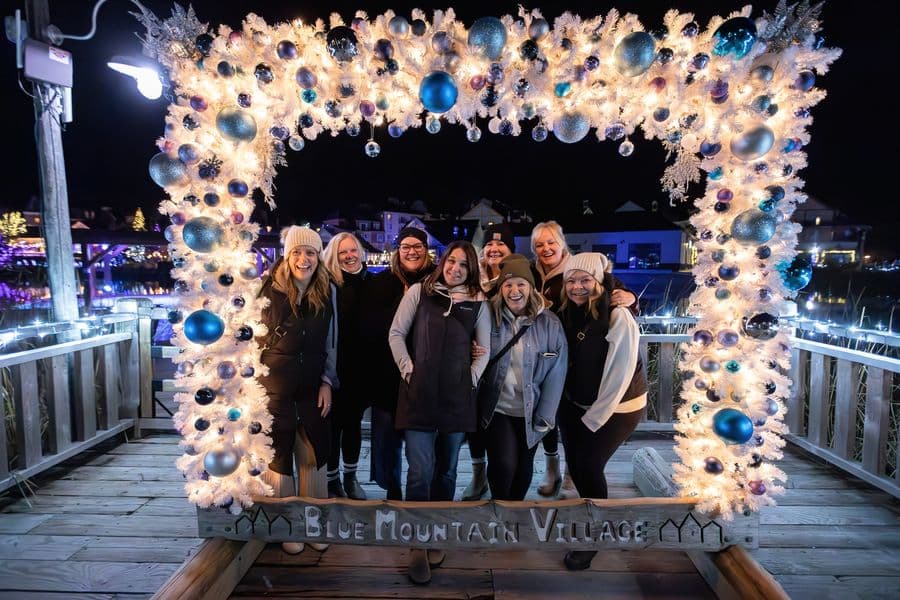 Group of colleagues gathered behind a festively lit and decorated photo frame for a holiday group photo.