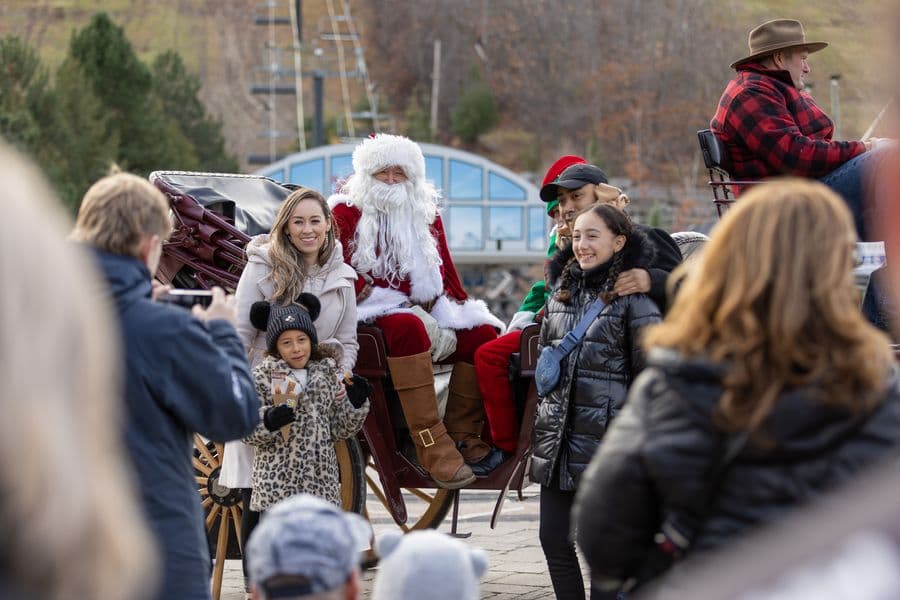 Family gathered around Santa and his horse-drawn carriage taking a family photo at the base of the Mountain.