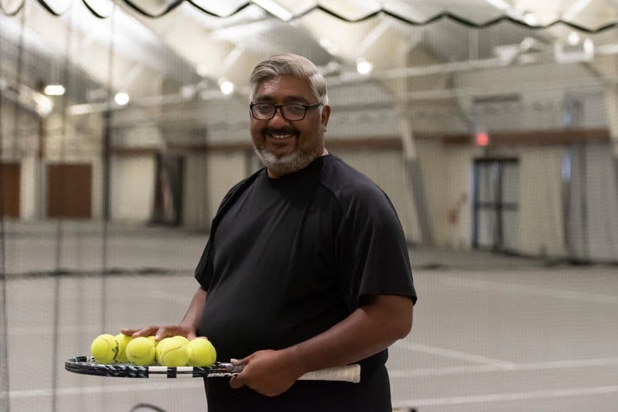 Man holding up a tennis racket topped with a handful of tennis balls at the state-of-the-art indoor tennis facility.