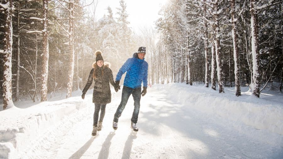 Couple holding hands and skating around the 1.1km ice skating loop at the top of the Mountain on a snowy winter's day.