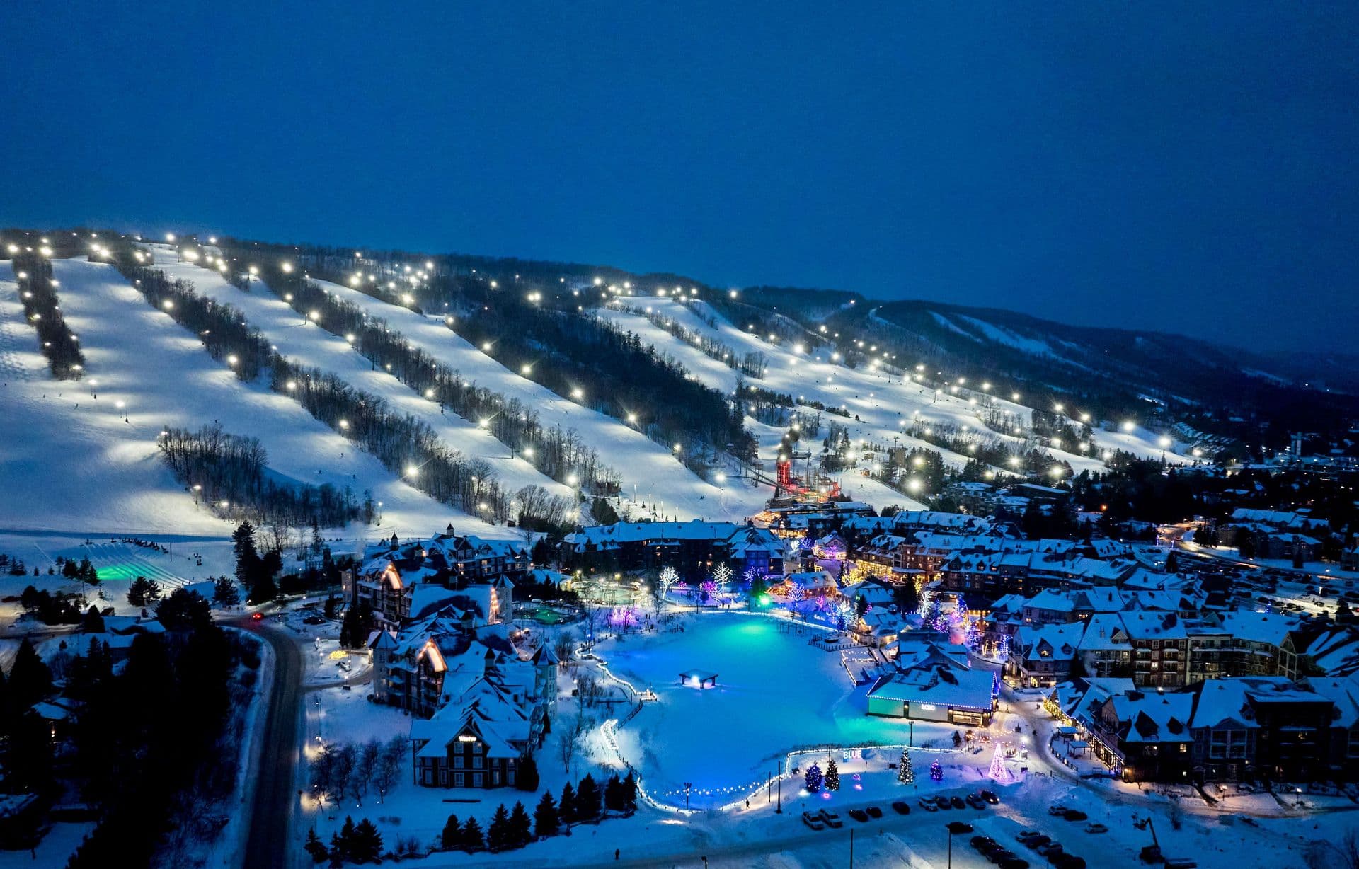 A nighttime aerial view of Blue Mountain and Village, showcasing the lit up slopes and Holiday Magic Light Trail.