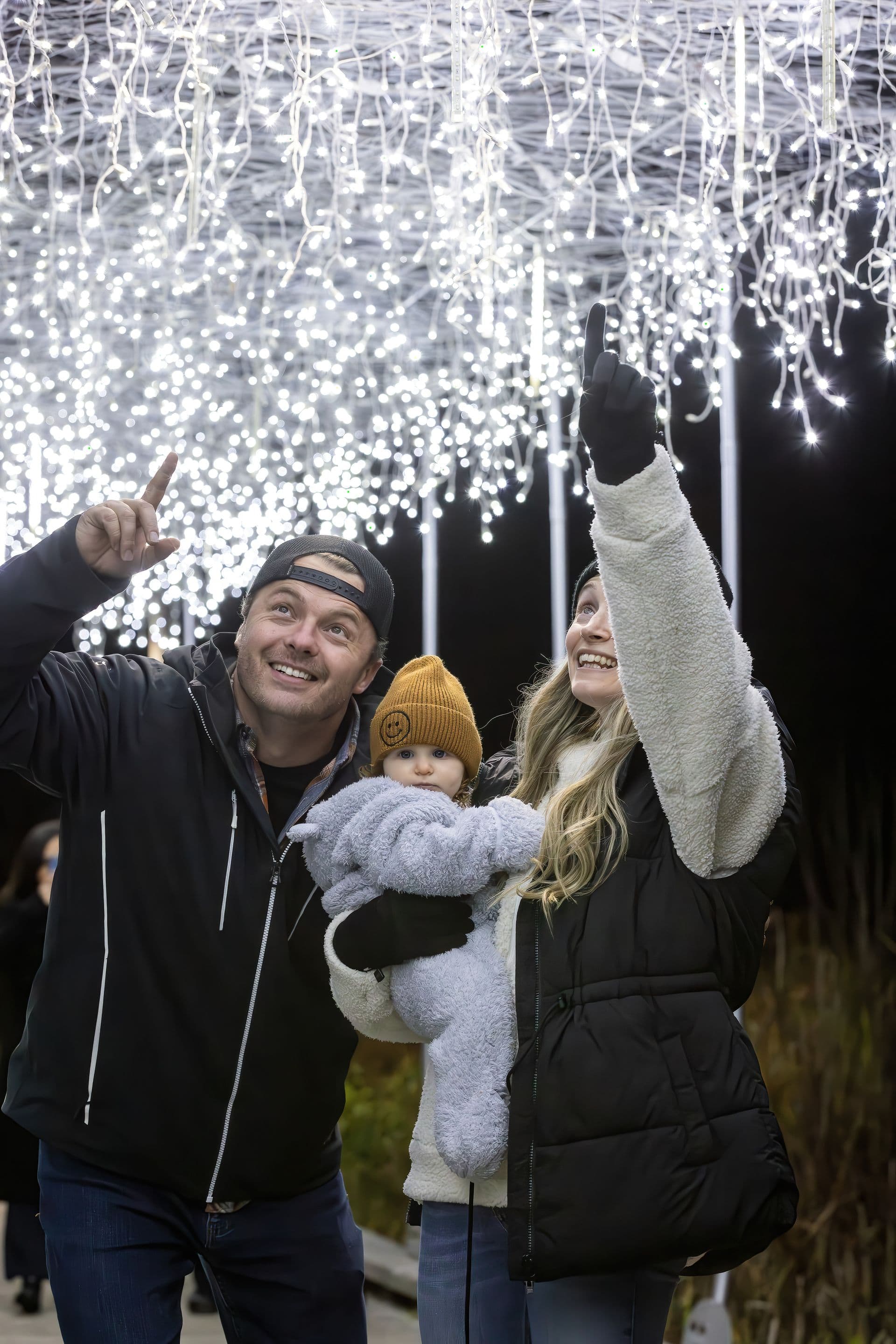 Parents with young baby pointing to show the baby the dangling Holiday Magic Lights.