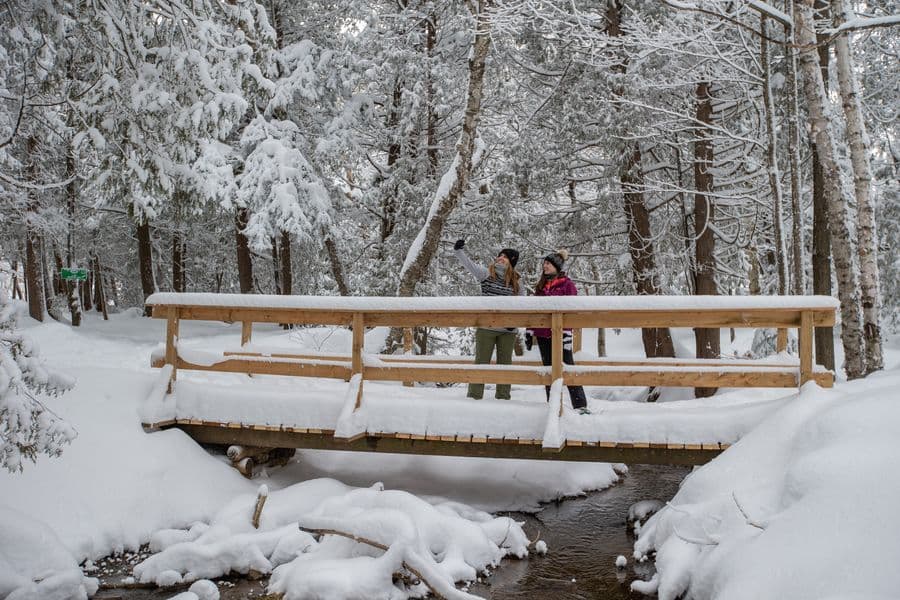 Two friends taking a selfie on the snow-covered bridge along the winter snowshoeing trail.