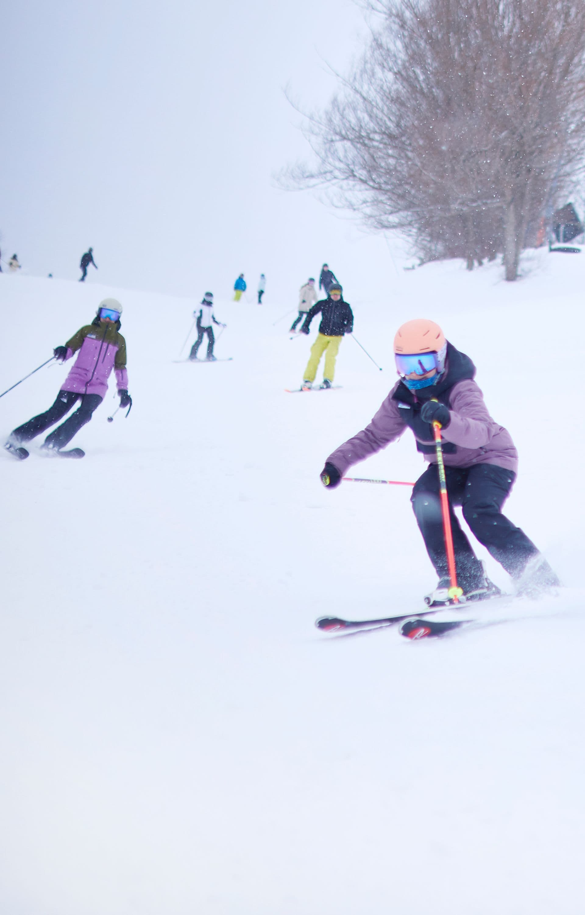 Group of friends race each other down the ski slopes on a snowy Winter afternoon.