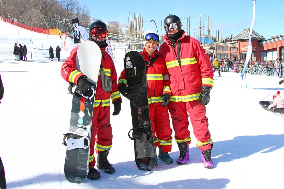 3 smiling snowboarders dressed in firefighter suits pose for a team photo at 24h Blue Mtn.