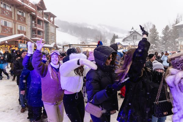 Group of people laughing and dancing in a conga line on a snowy afternoon.