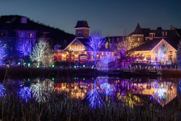 A dazzling view of the Holiday Magic Light Trail with trees and buildings decorated with lights, reflecting across the Mill Pond.