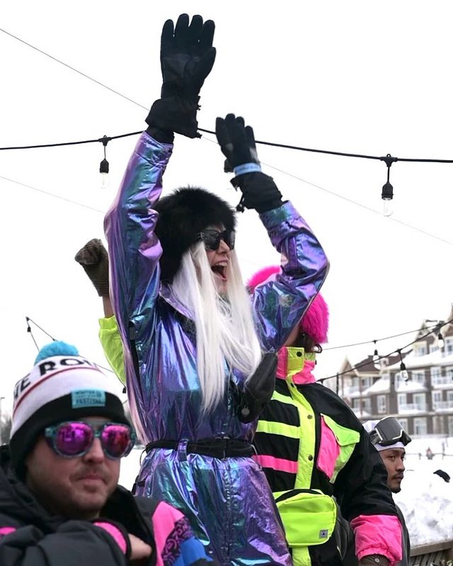 Girl dressed in retro/neon Apres attire, dancing with hands in the air on Kaytoo's patio during the Aftrglow Festival in 2025